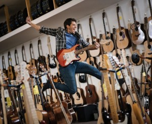 Man jumping while playing electric guitar in guitar shop